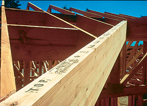 A straight glued-laminated timber (glulam) ridge beam installed in a wood-framed roof, the horizontal glue lines between laminations clearly visible along its face